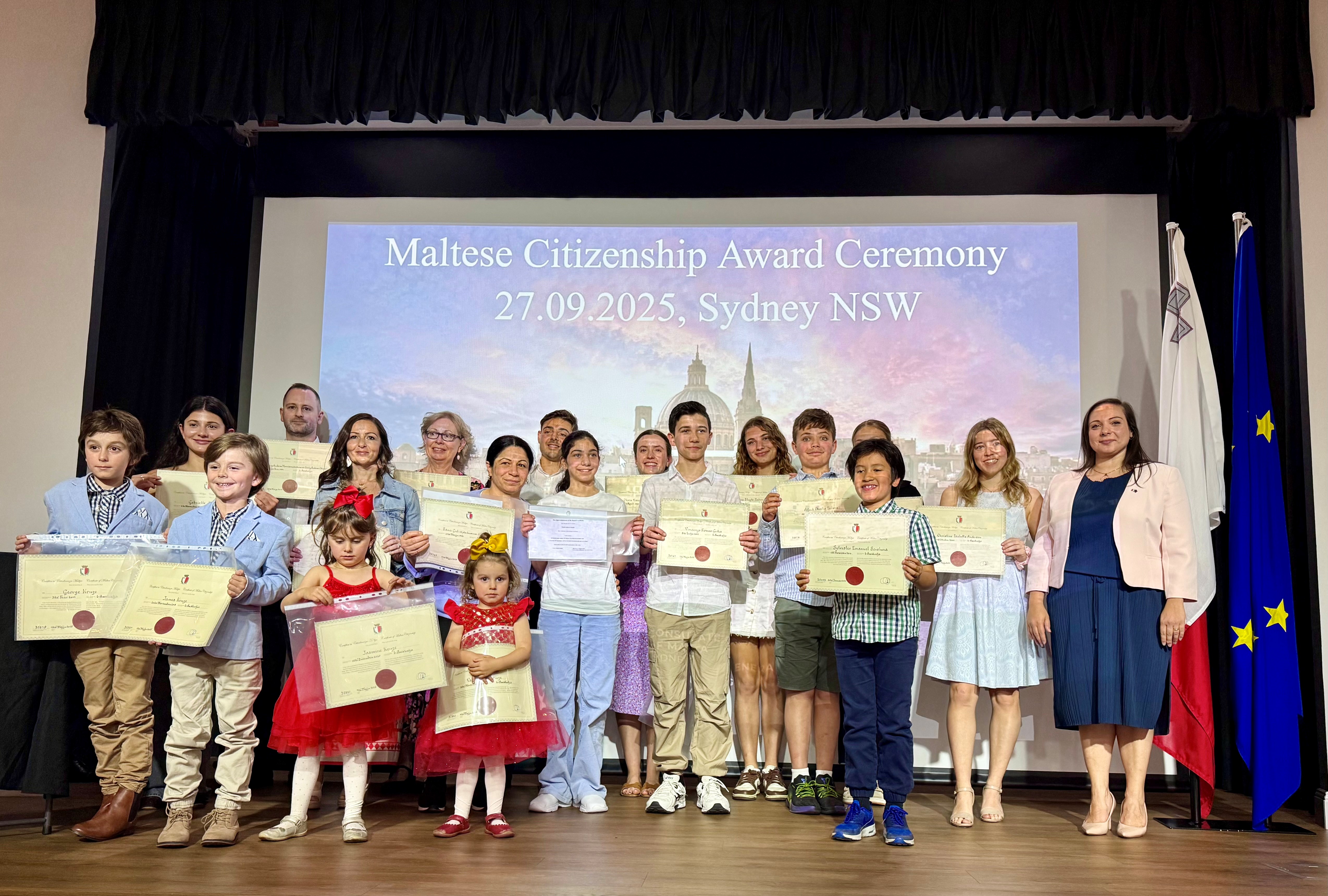 Group photo of new Maltese citizens holding their certificates during the Maltese Citizenship Award Ceremony in Sydney, NSW. The Consul General of Malta in Sydney stands with the recipients.