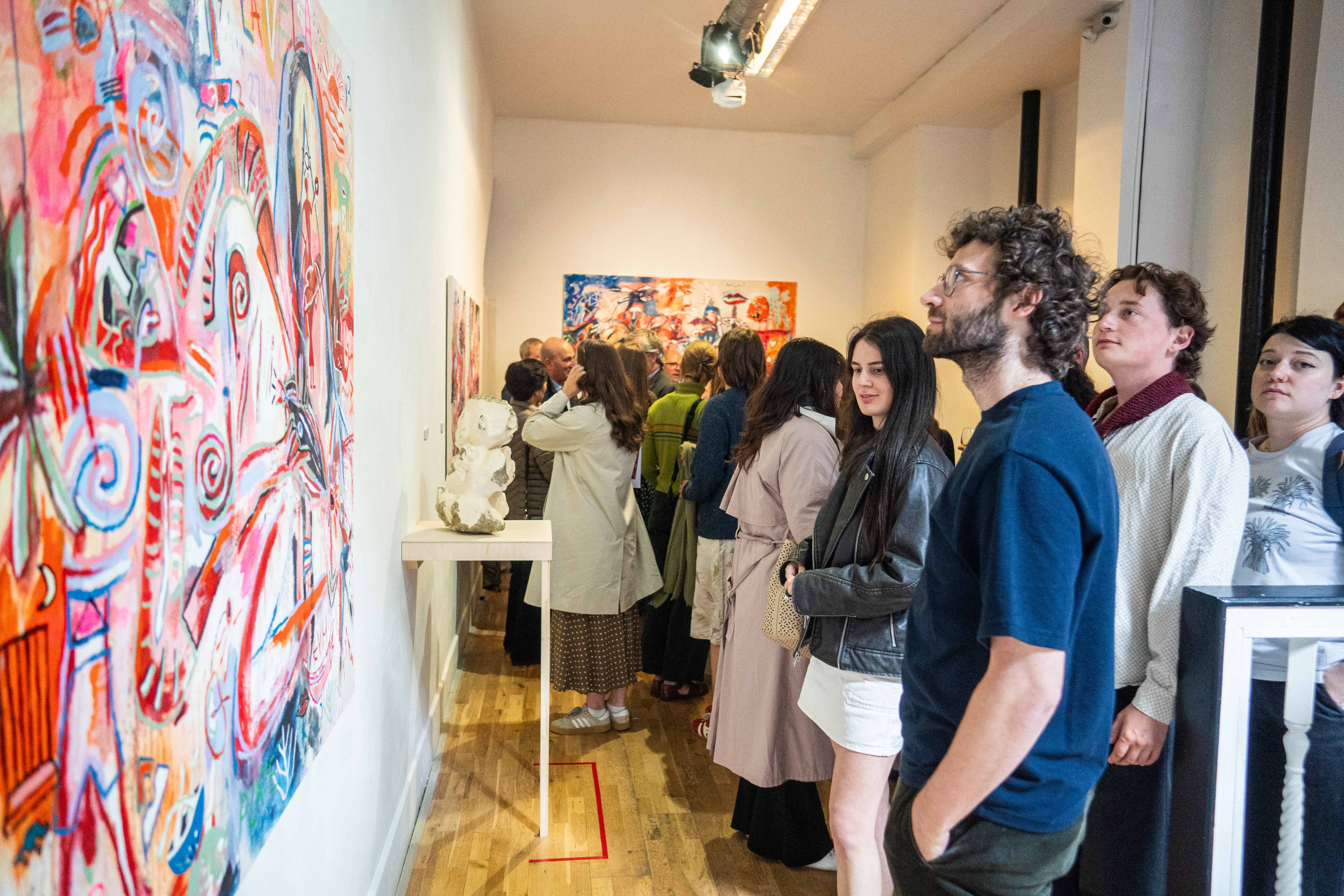 Attendees at the exhibition launch look at an abstract multicoloured painting on the wall. 