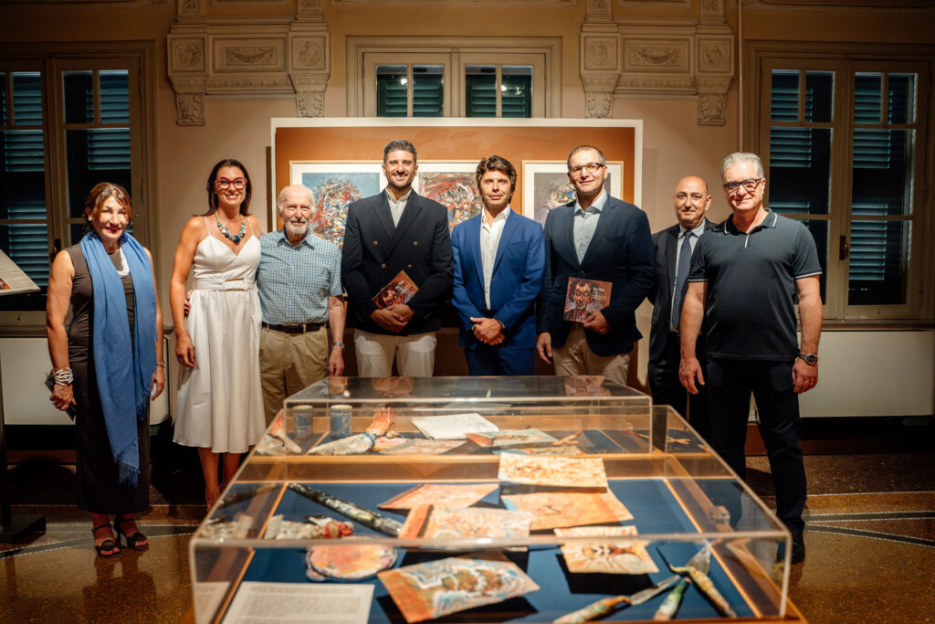 Inauguration of the exhibition; a group of eight individuals standing in a row. From left: Ms Annabelle Stivala, Director for International Cultural Relations & Events; Ms Cinzia Grech; Prof. Kenneth Wain; Dr. Luke Dalli, Executive Chairperson of Arts Council Malta; H.E. Daniel Azzopardi, Ambassador of Malta to Italy; Mr Christopher Cutajar, Permanent Secretary at the Ministry for Foreign and European Affairs; Dr Sandro Debono, Curator of the exhibition; and Mr Daniele Pitré.