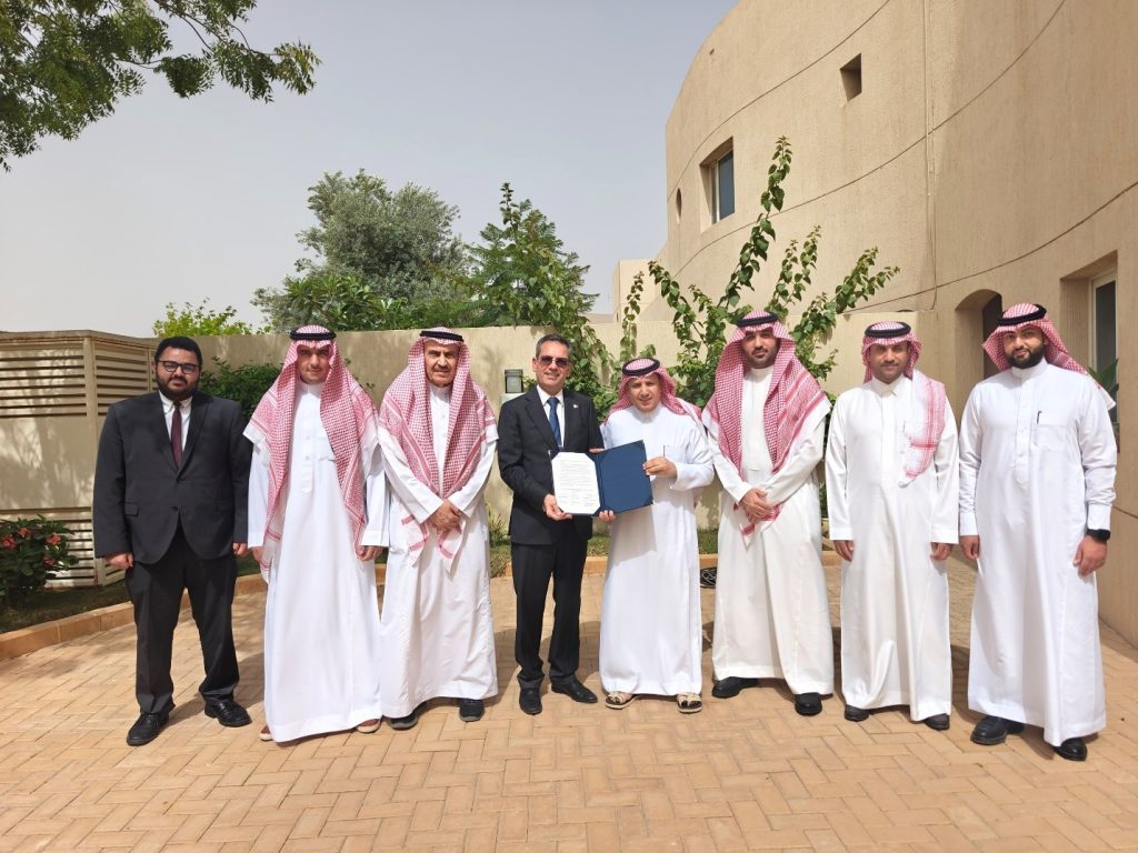 A group of men, six in traditional attire and two in jacket and tie, proudly holding a certificate, celebrating their achievement together